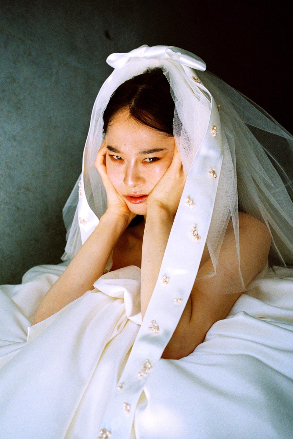 A woman in a wedding dress and veil rests her chin on her hands.