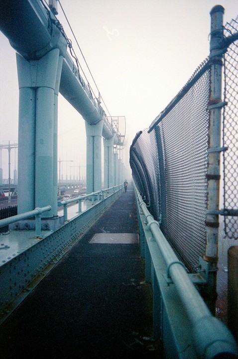 A person walks along a pedestrian path on a bridge on a foggy day.