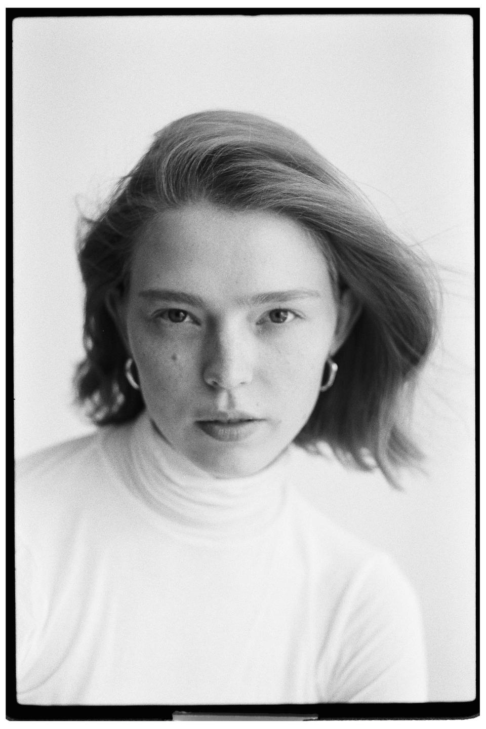 A woman with short hair and a turtleneck looks directly at the viewer.