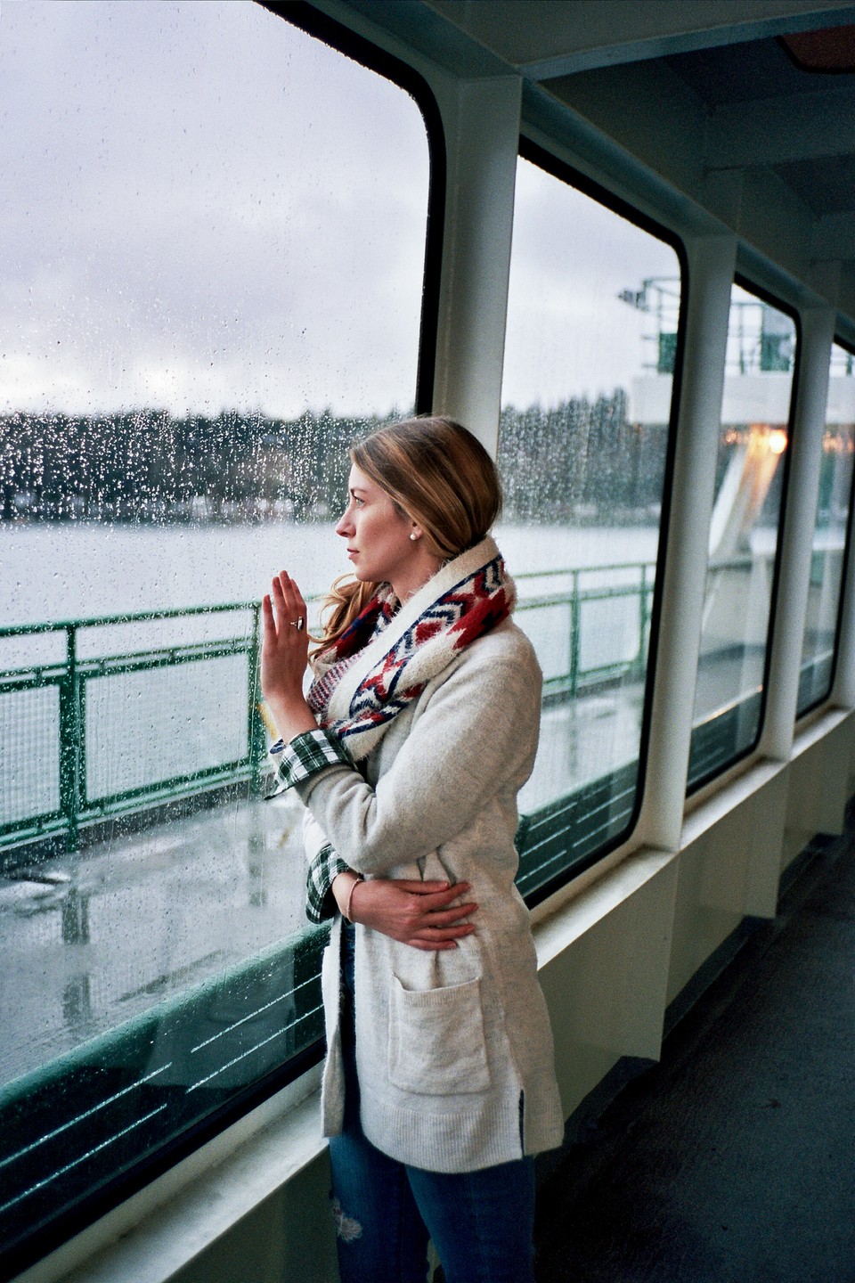 A woman looks out a rain-streaked window on a boat.