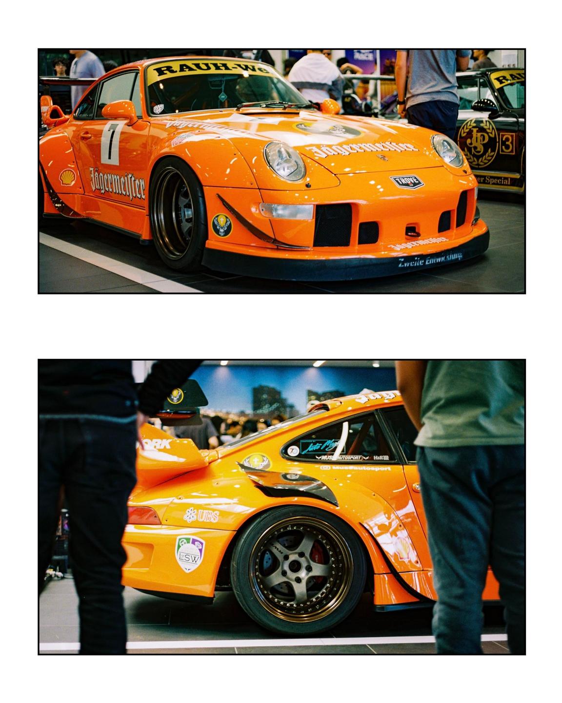 An orange Porsche 993 with Jägermeister livery is parked indoors, with people standing around it.