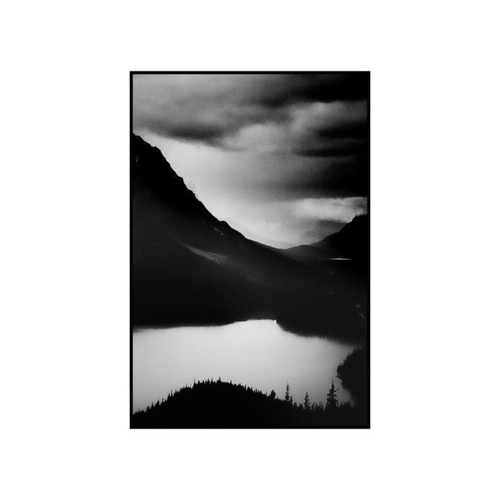 A black and white landscape shows a lake surrounded by mountains under a cloudy sky.