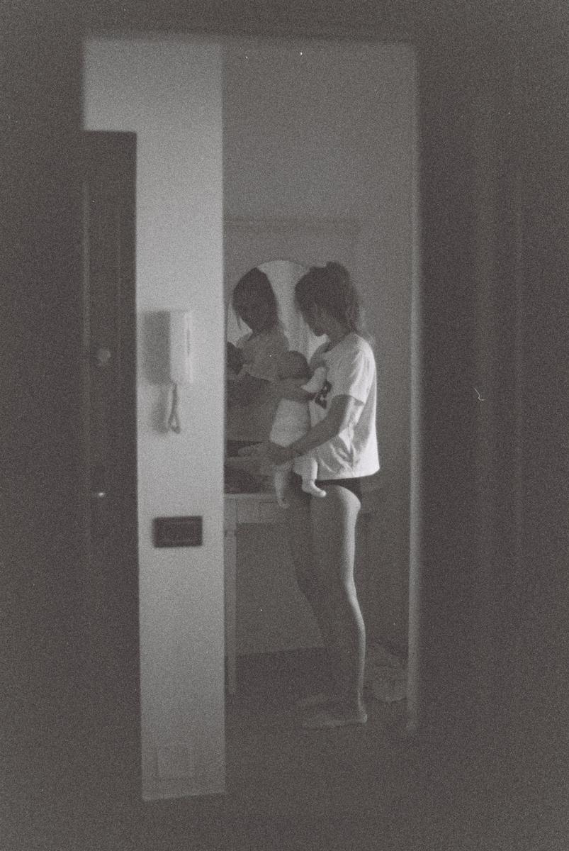 A woman holds a baby in a room with a mirror reflecting their figures.