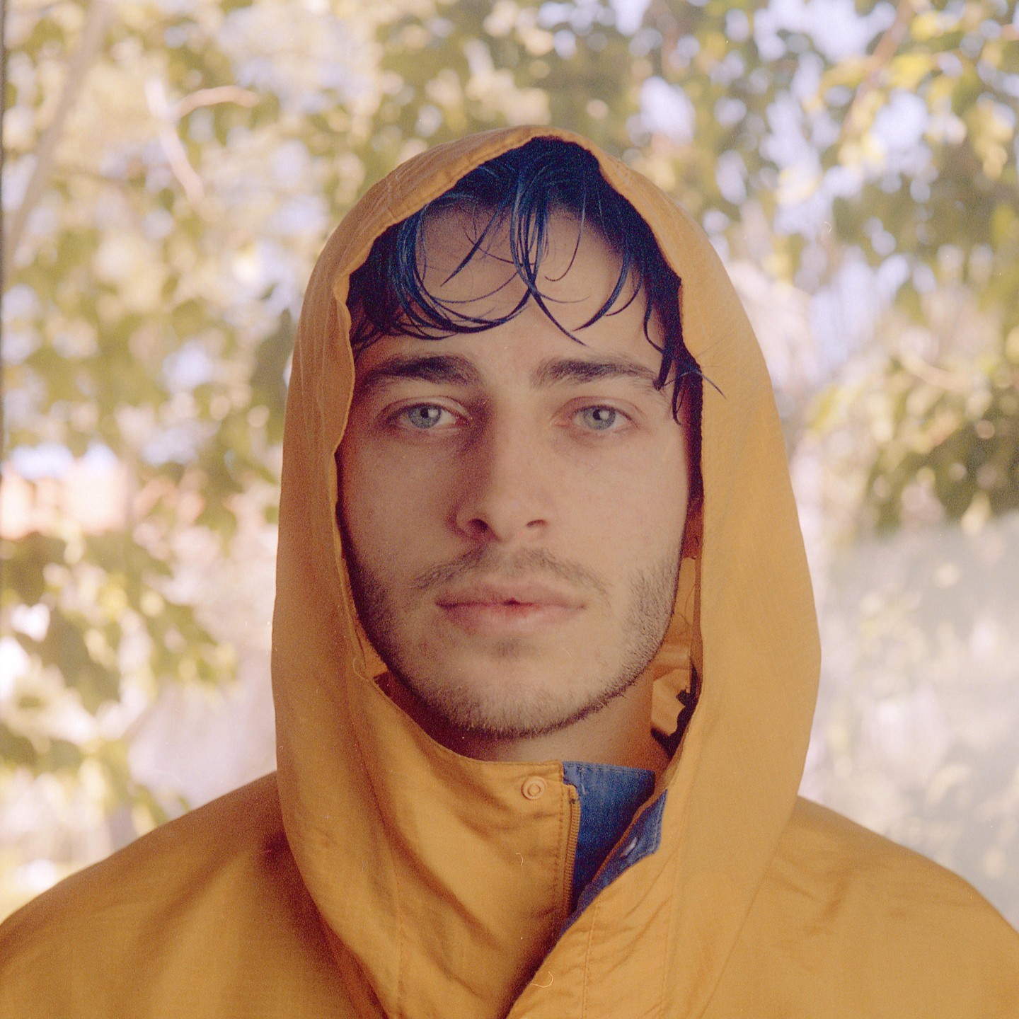 A man with wet hair looks directly at the viewer while wearing a yellow hooded jacket.