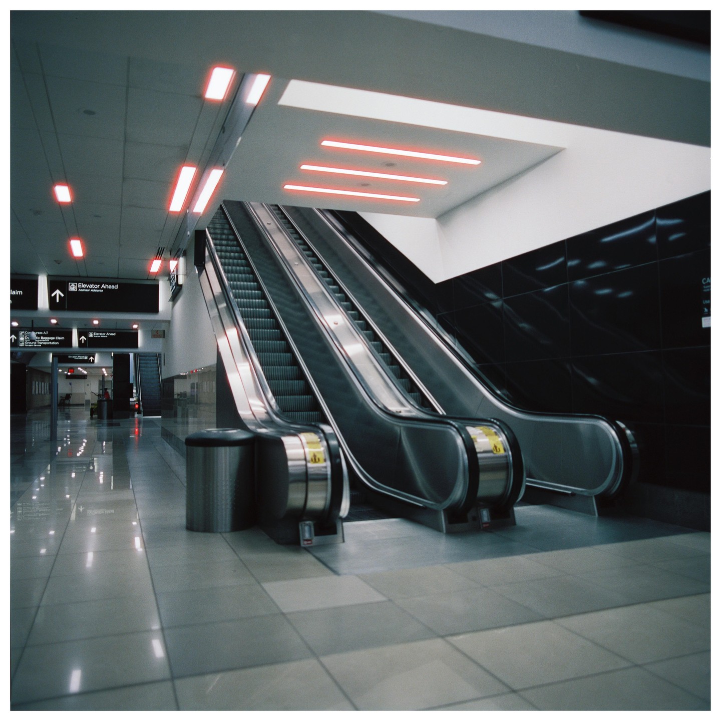 Two escalators ascend towards a ceiling with red neon lights in an airport.