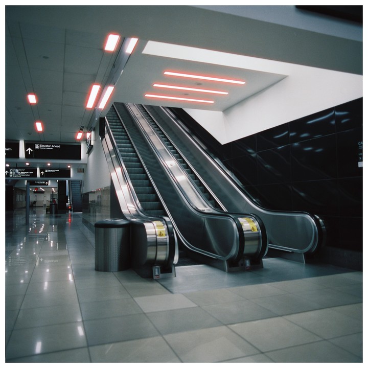 Two escalators ascend towards a ceiling with red neon lights in an airport.