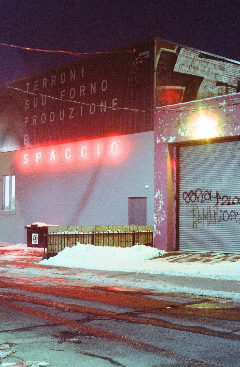 A building with a neon sign that says "SPACCIO" is covered in snow at night.