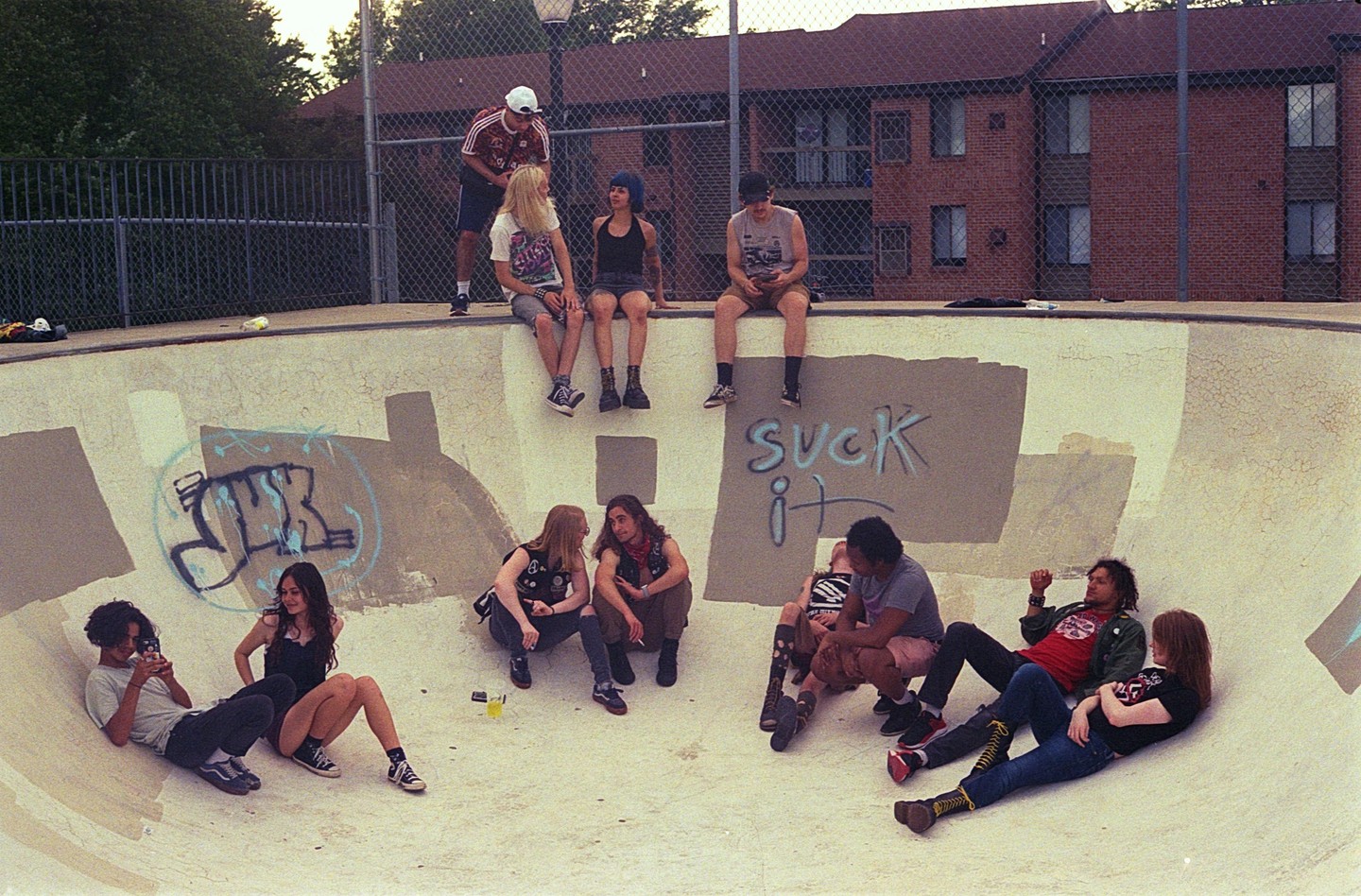A group of young people are hanging out in a skatepark with graffiti on the walls.