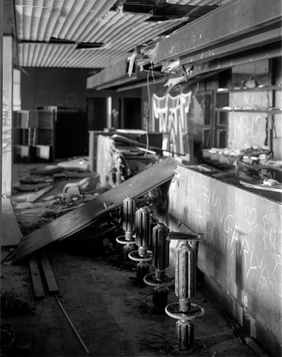 Four bar stool bases stand in front of a graffiti-covered counter in a derelict room.