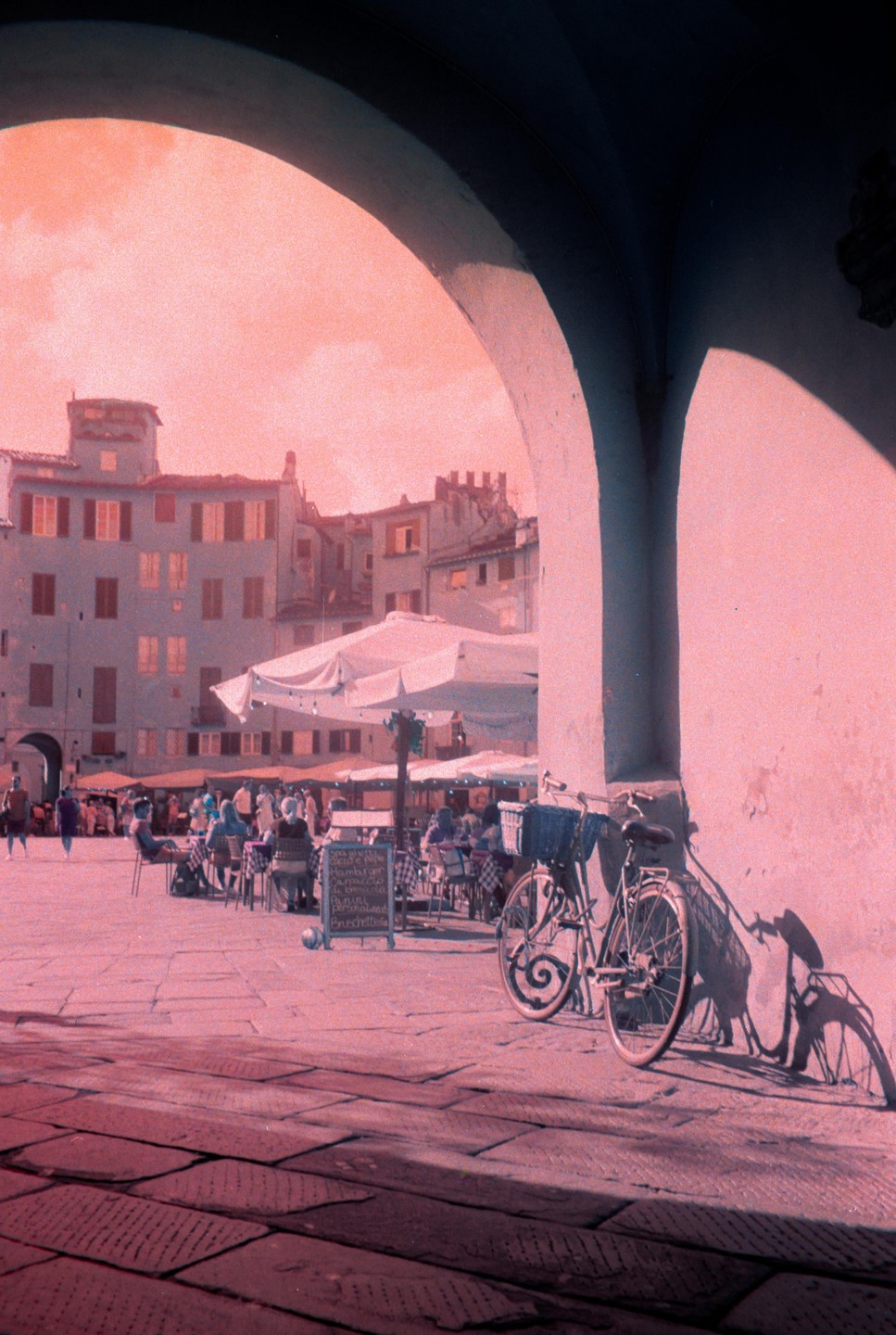A bicycle leans against an archway overlooking a bustling outdoor cafe in a town square.