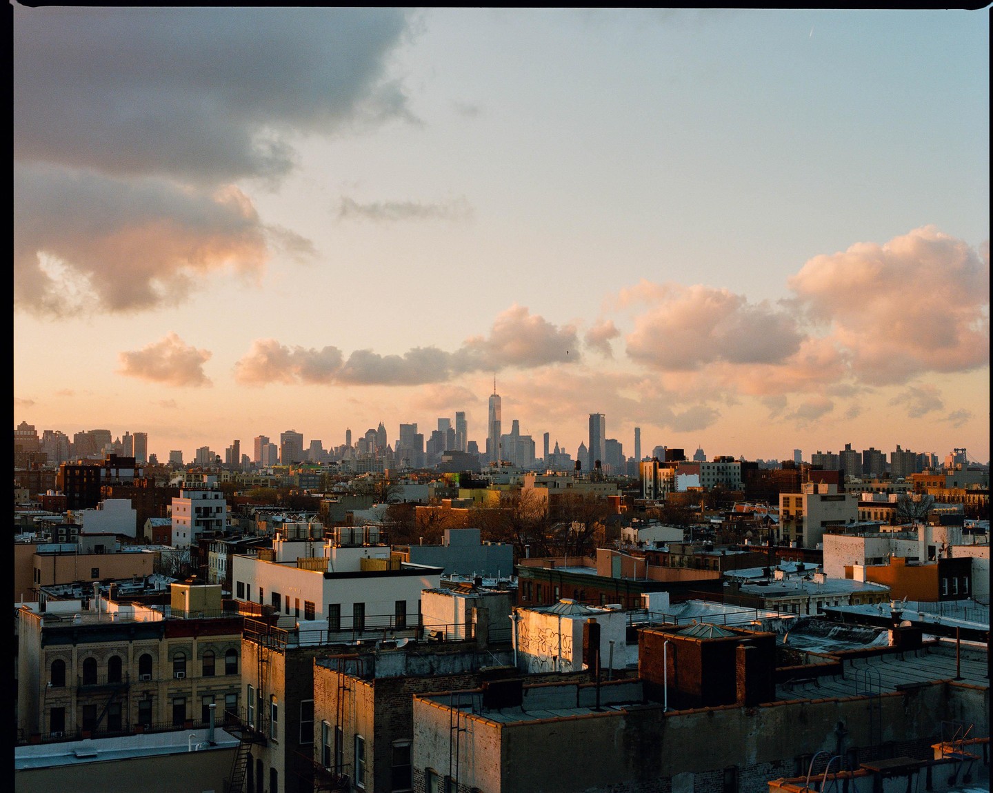 A cityscape with many buildings and a cloudy sky at sunset.