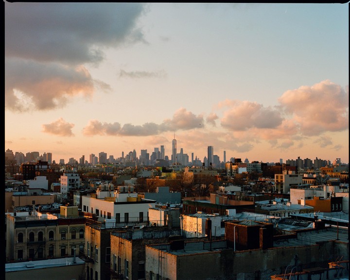 A cityscape with many buildings and a cloudy sky at sunset.