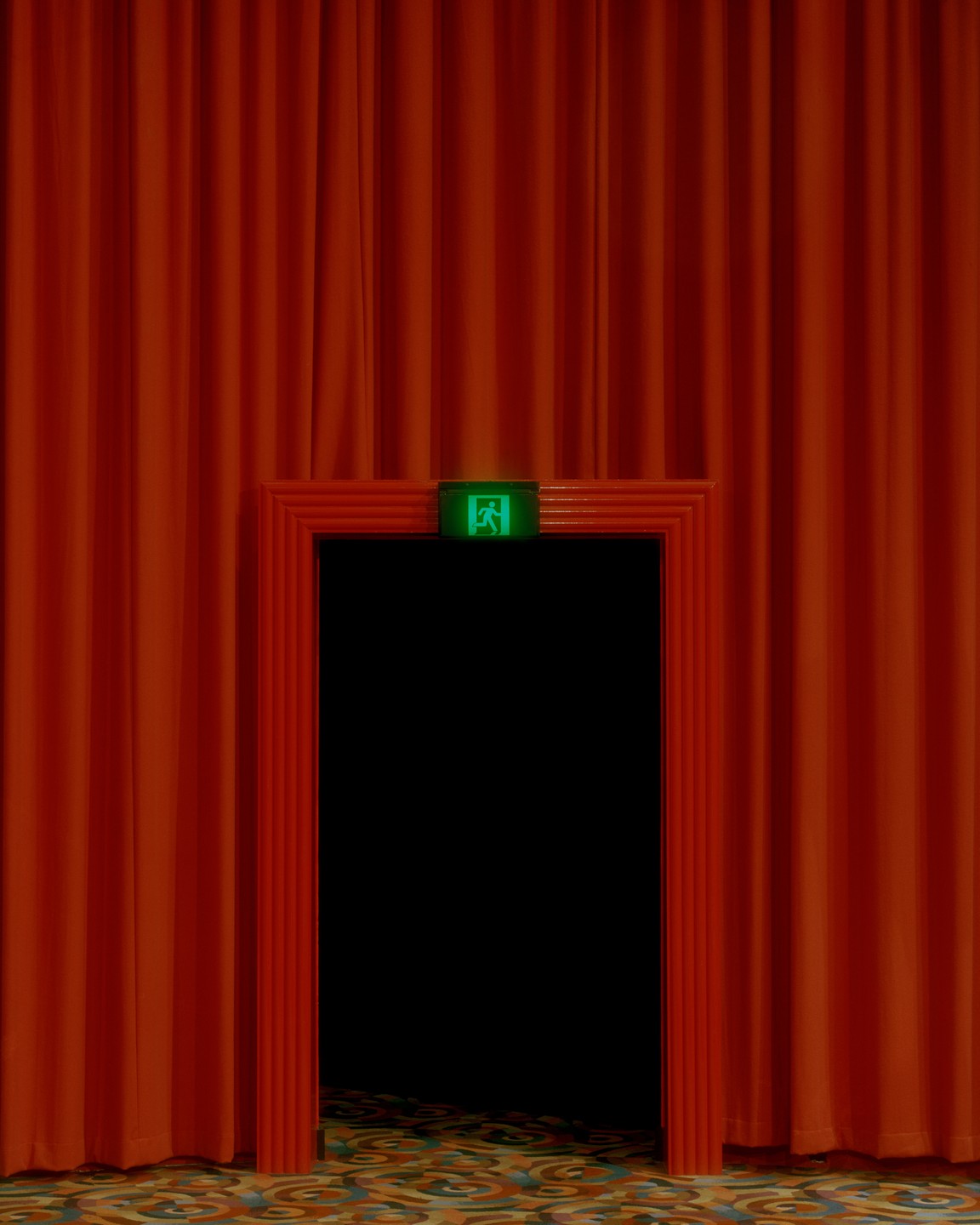 A green exit sign is visible above a dark doorway framed by red curtains and a patterned carpet.