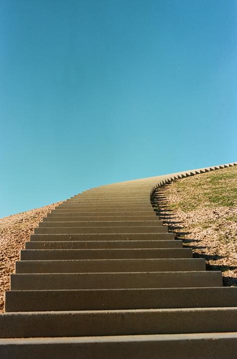 A long concrete staircase ascends a grassy hill under a clear blue sky.