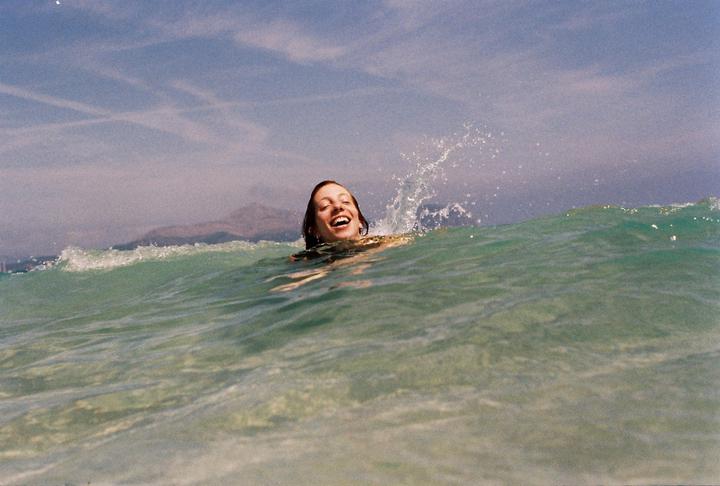 A woman with a joyful expression is in the ocean with water splashing around her.