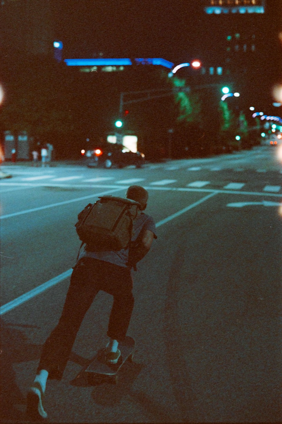 A man with a backpack rides a skateboard down a city street at night.