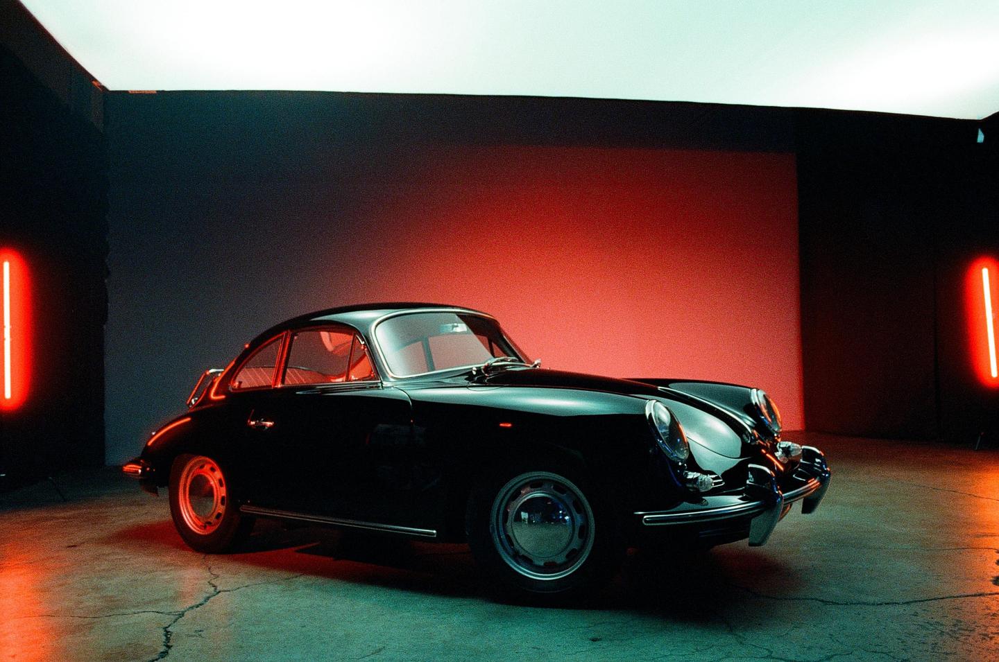 A black vintage car is parked in a studio with red and blue lighting.