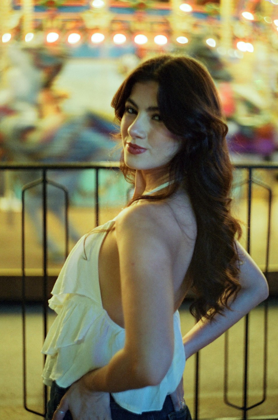 A woman with long, dark hair looks over her shoulder at the viewer, with a blurred background of colorful lights.