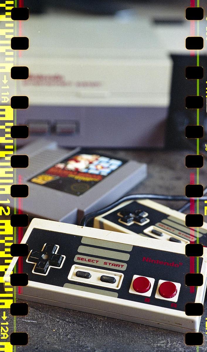 A Nintendo Entertainment System console, game cartridge, and two controllers are arranged on a dark surface.