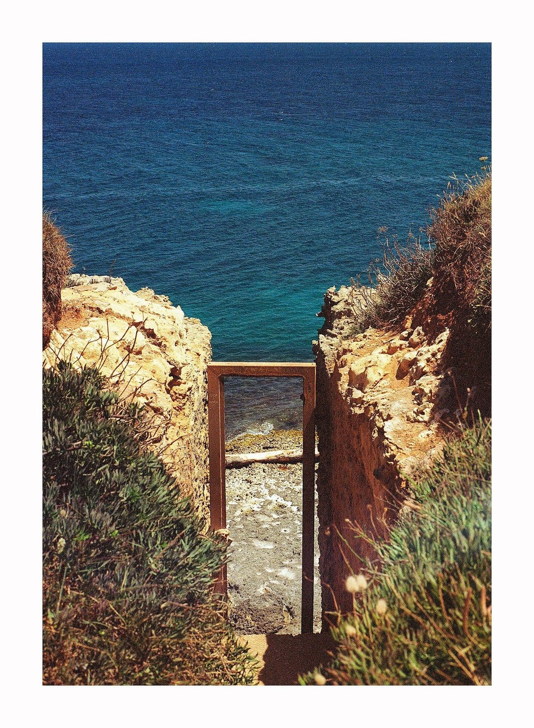 A wooden frame stands between two rocky cliffs, looking out onto the ocean and a small beach.