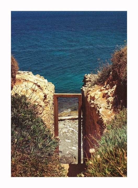 A wooden frame stands between two rocky cliffs, looking out onto the ocean and a small beach.