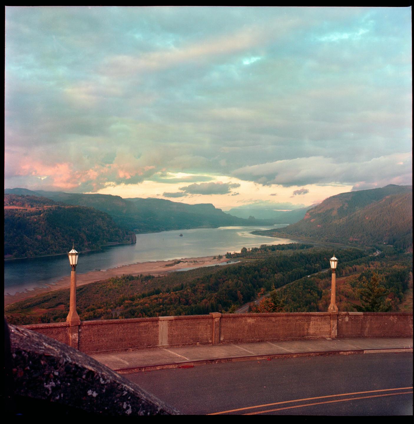 A wide river flows through a gorge with forested hills under a cloudy sky.