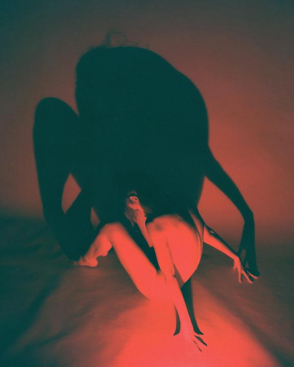 A woman sits on the floor with a large shadow behind her.