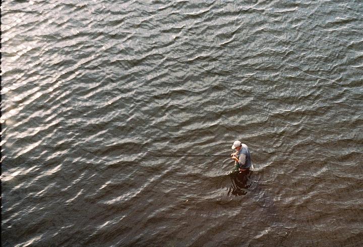 A man stands in the water holding a fishing rod.