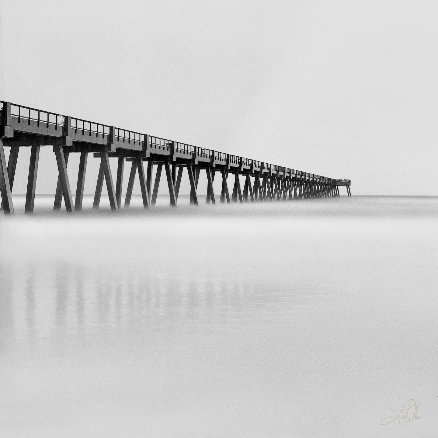 A long pier extends into the distance over calm water under a bright sky.