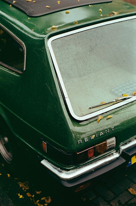 The rear of a green Reliant car is covered in raindrops and a few autumn leaves.