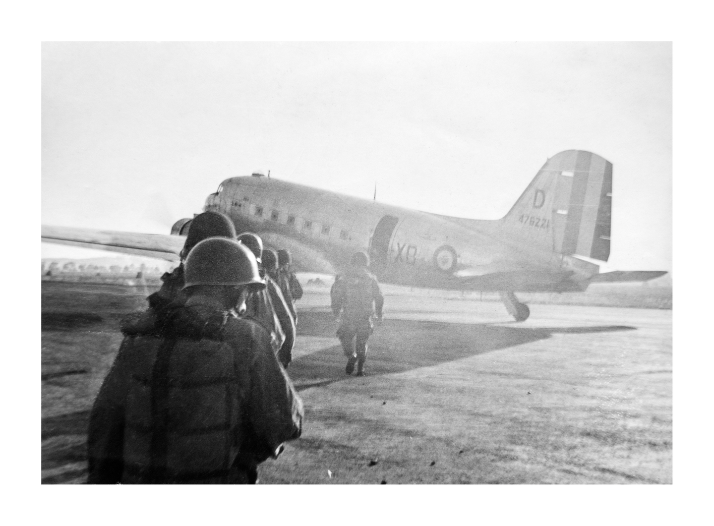 A group of soldiers in uniform and helmets walk towards a large airplane on an airfield.