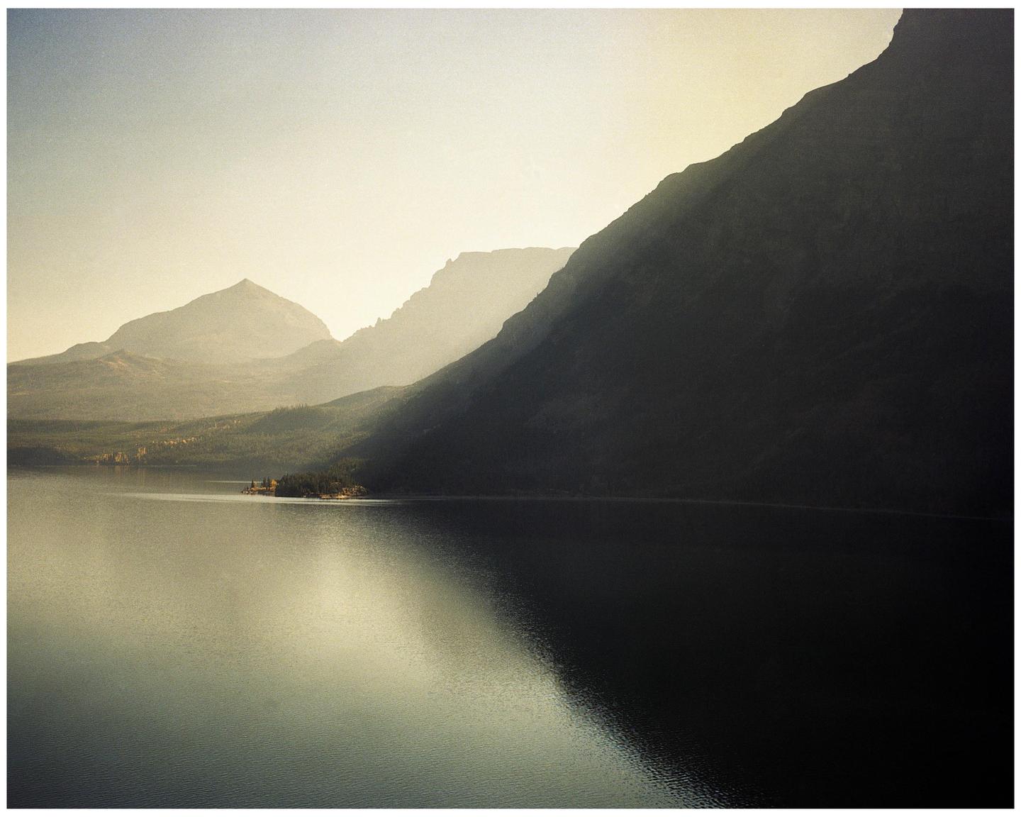 A hazy morning light illuminates a lake and mountains in Glacier National Park.
