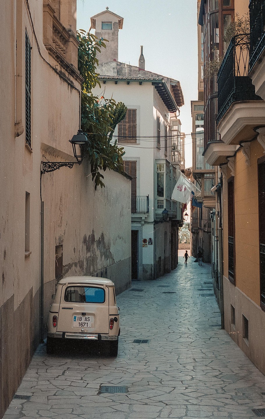 A small white car is parked on a narrow cobblestone street lined with tall buildings.