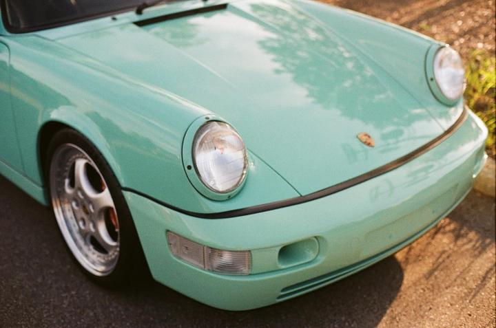A mint green car with round headlights is parked on asphalt.