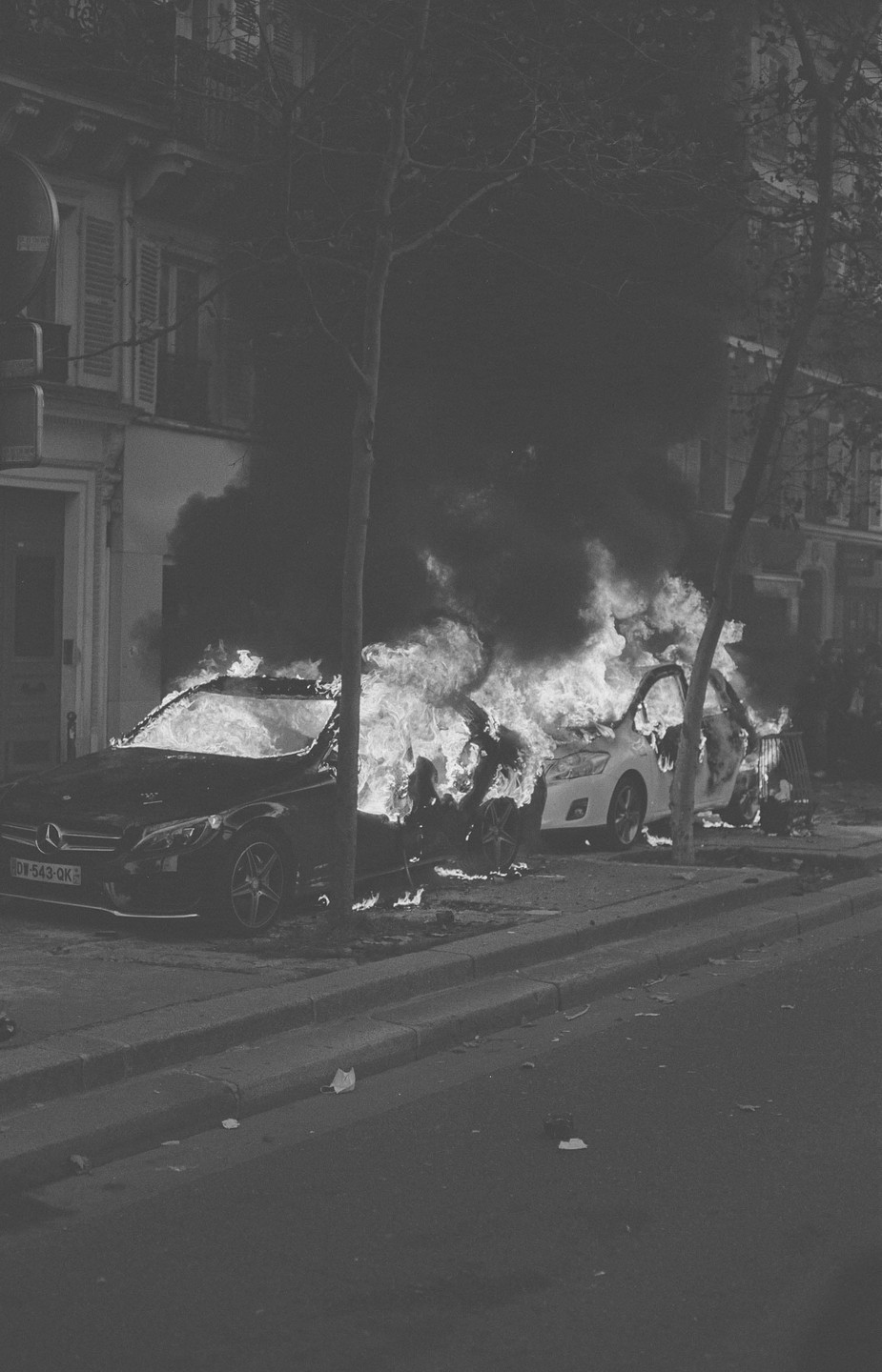 Two cars are engulfed in flames and smoke on a city street at night.
