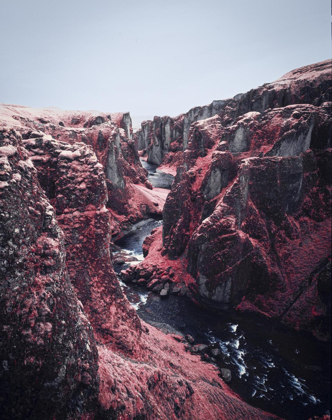 A river flows through a canyon with red foliage and snow-dusted rocks.