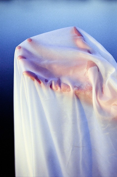 A hand is visible through a translucent white fabric against a blue background.