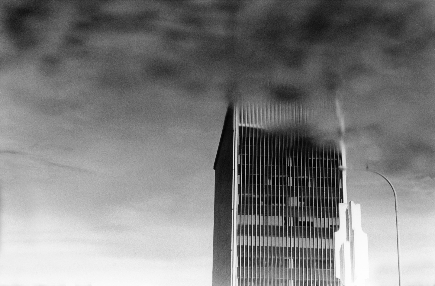 A tall building with many windows is partially obscured by a dark, blurry cloud-like shape.