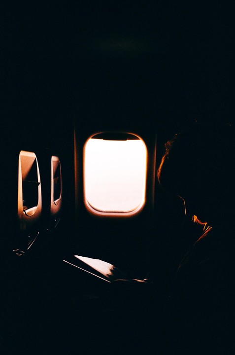 A person reads a book next to an airplane window.