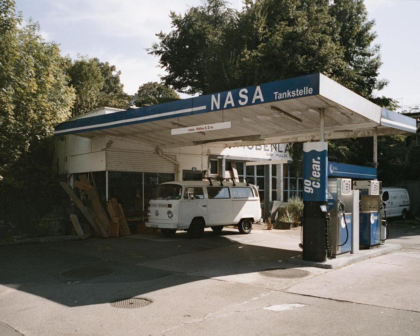 A white van is parked at a gas station with a "NASA Tankstelle" sign.