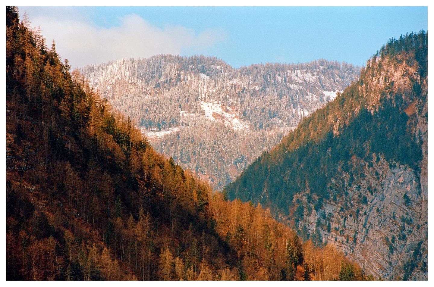 Three mountains with different vegetation stages are visible under a blue sky.