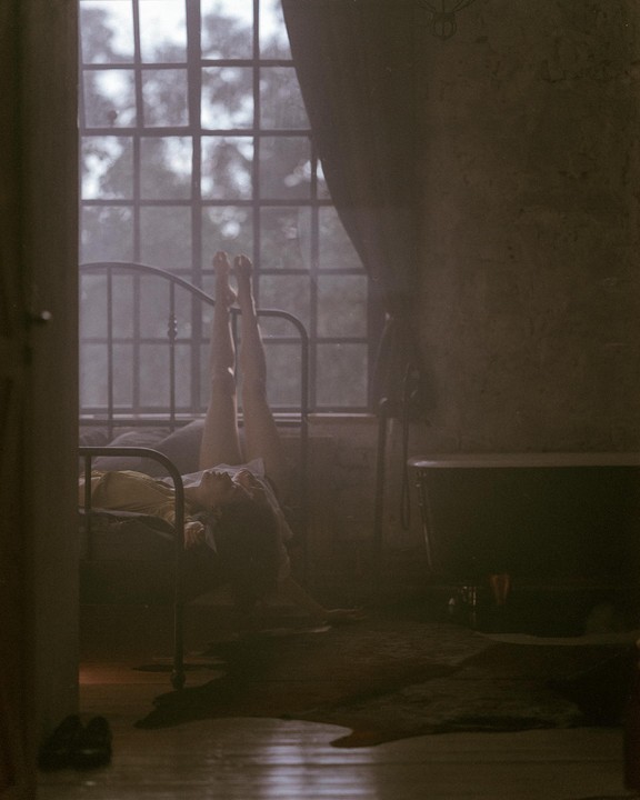 A woman lies on a bed with her legs up against a window.
