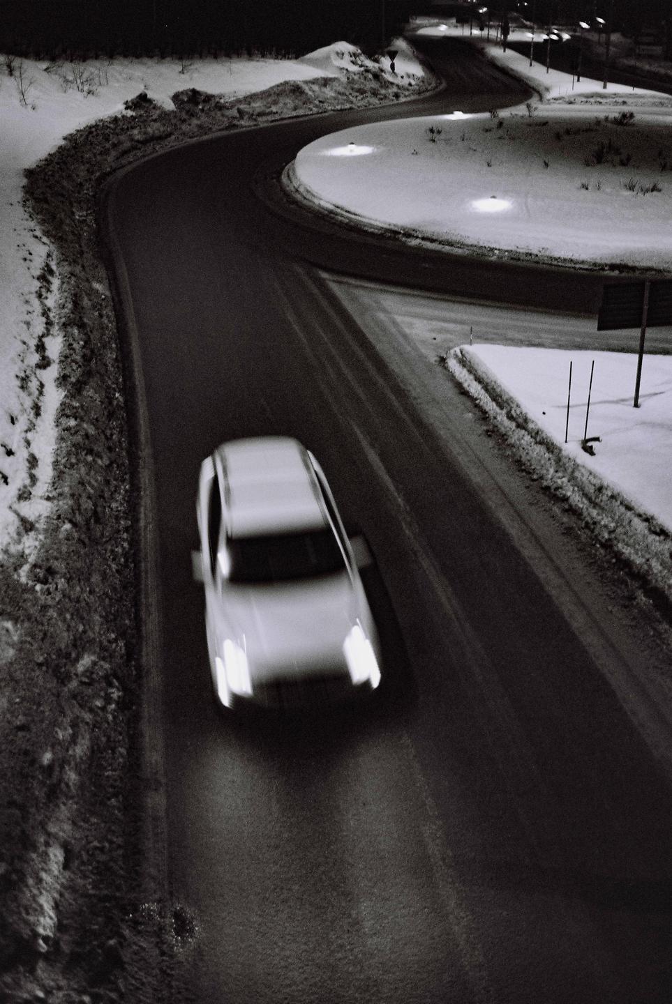 A car drives along a winding road covered in snow at night.