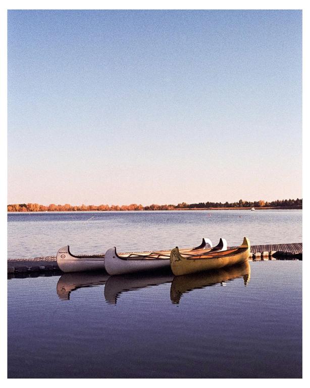 Three canoes are docked on a calm lake with a distant shoreline under a clear sky.