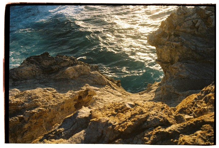 The sun reflects on the ocean waves next to a rocky cliff.