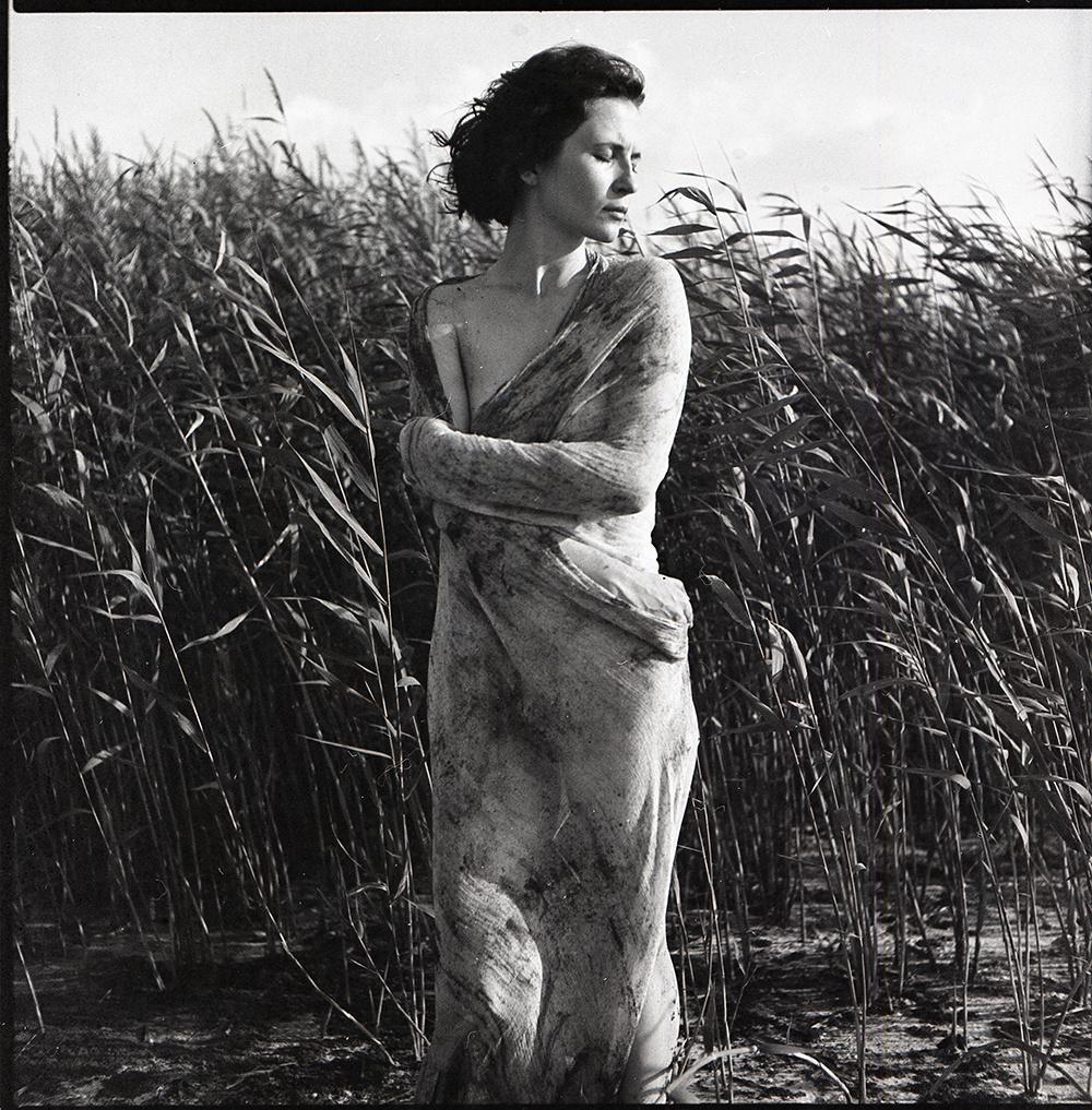 A woman wrapped in fabric stands in a field of tall reeds.