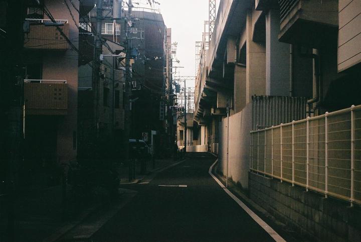A narrow street is flanked by buildings and an elevated structure, with utility poles and wires visible on the left.