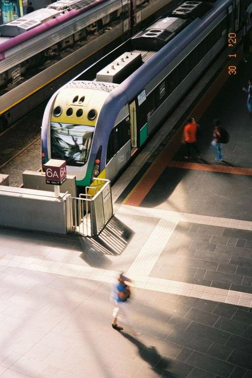 A train is stopped at a station platform with people walking nearby.
