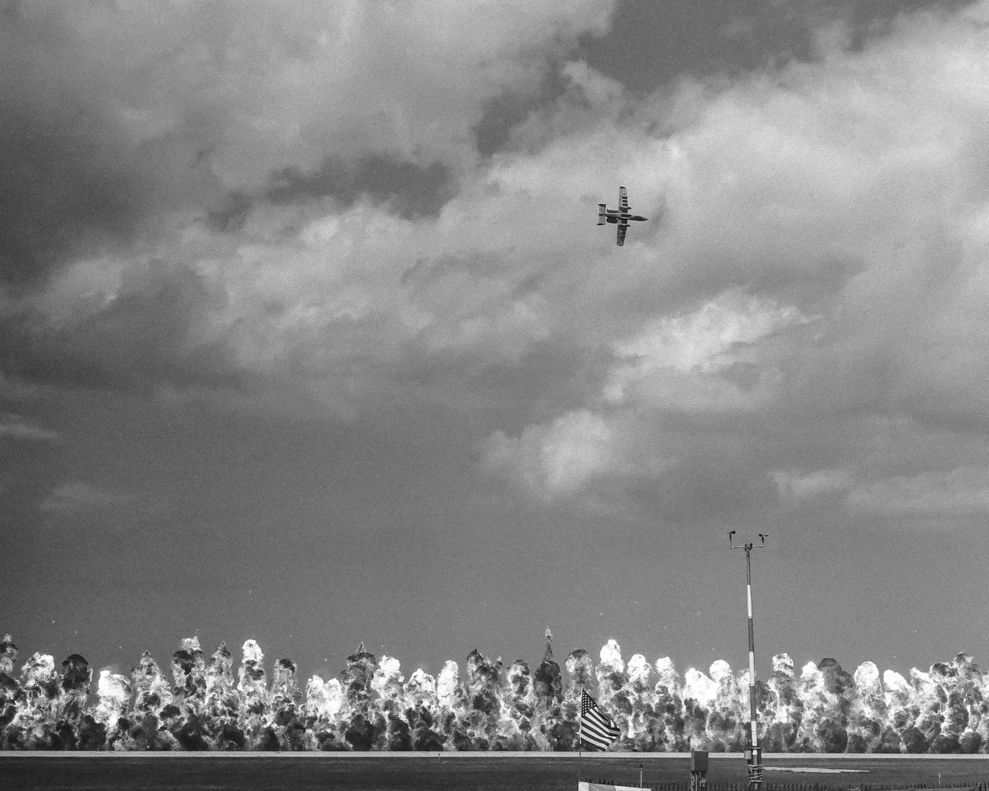 A jet flies over a field with explosions and an American flag.