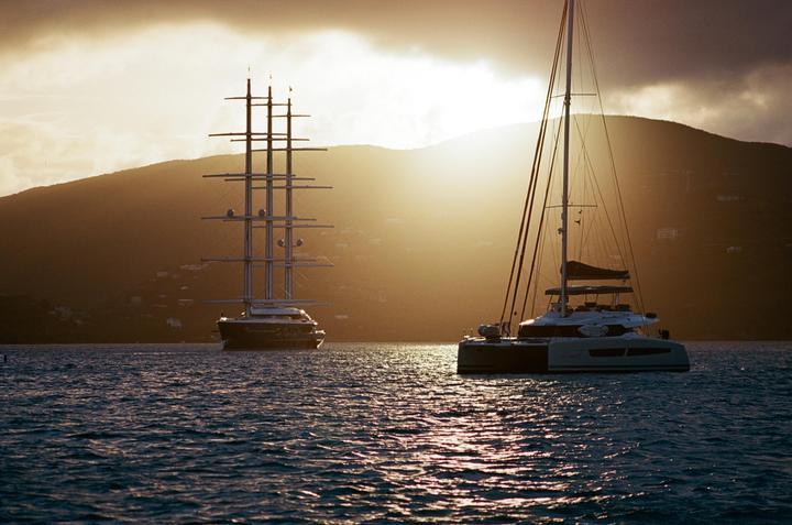 Two boats are on the water with a mountain and a bright sky in the background.